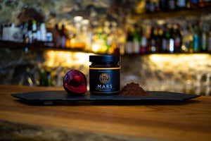 Mars Fruchtaufstrich Pflaume Kakao auf einem schwarzen Schiefertablett neben einer Pflaume und Kakaopulver